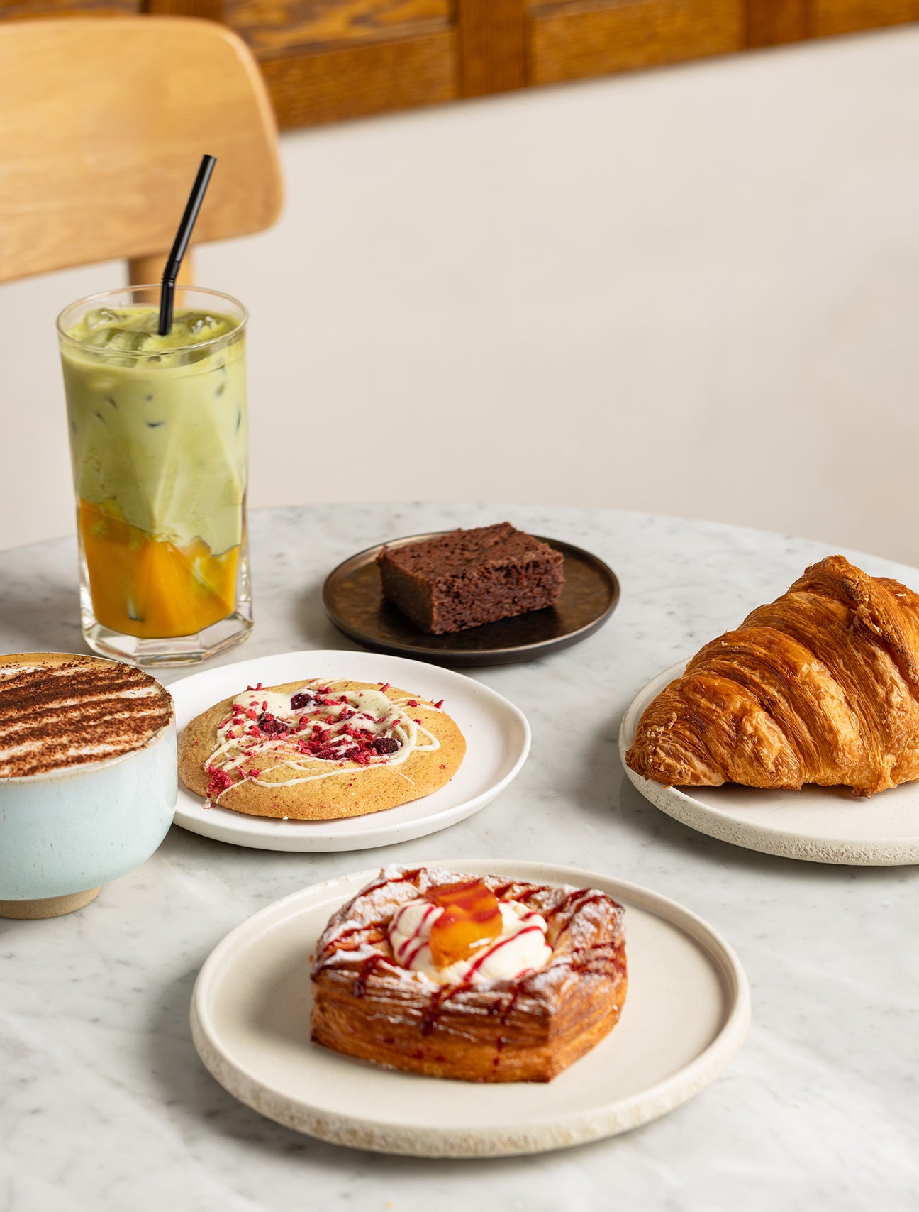 Assorted pastries and a drink on a marble surface with a wooden chair in the background.