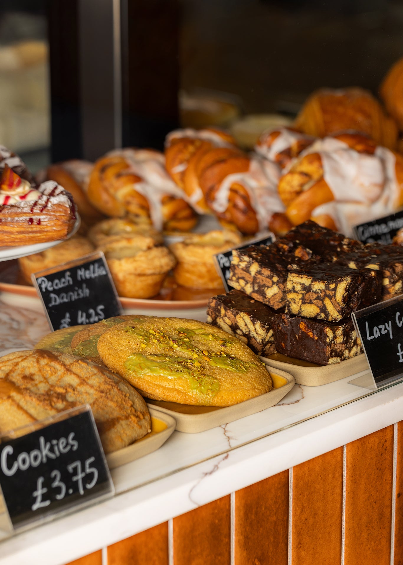 Display of pastries and cakes with price signs on a wooden counter.
