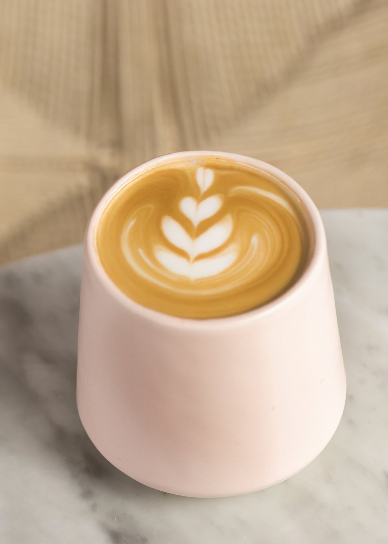 Pink ceramic cup with a latte art design on a neutral background