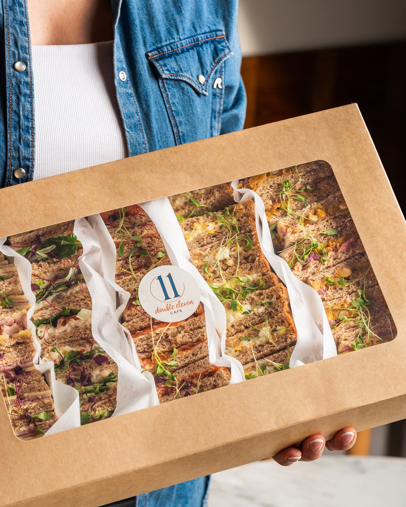 Person holding a box of sandwich selection with a visible brand logo.